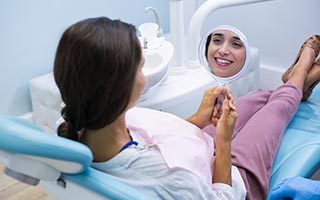 Smiling woman looking at mirror while sitting on dentist chair at clinic